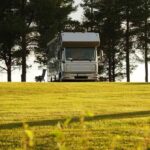 Caravan sur un champ herbeux entouré d'arbres sous un ciel ensoleillé