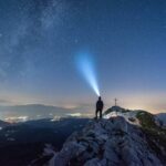 Silhouette d'une personne sur une montagne, un phare de lumière dans le ciel nocturne étoilé