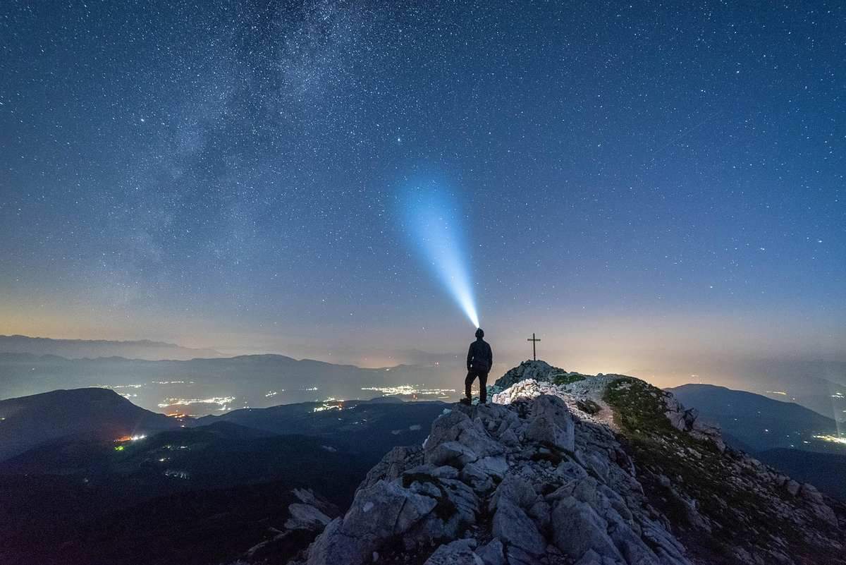 Silhouette d'une personne sur une montagne, un phare de lumière dans le ciel nocturne étoilé