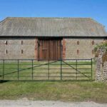 Grange en pierre avec toit métallique, porte en bois, portail fermé, pelouse verte