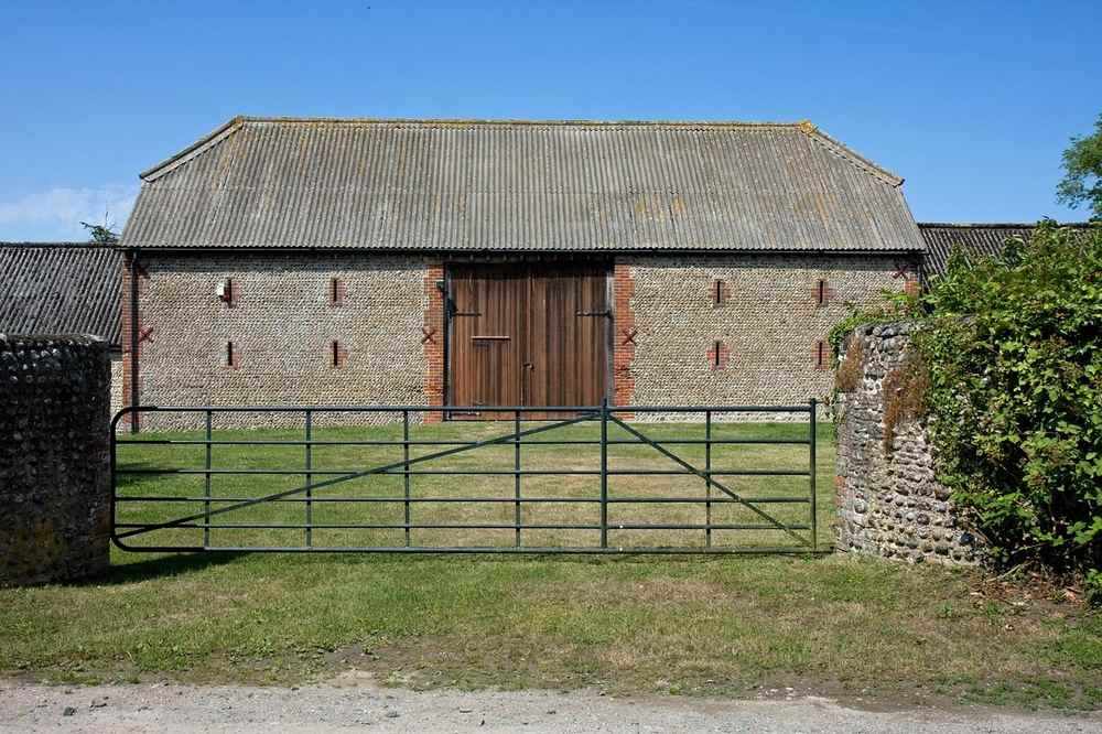 Grange en pierre avec toit métallique, porte en bois, portail fermé, pelouse verte